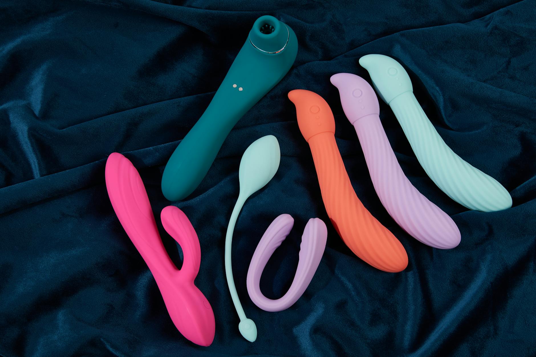 Vibrador de silicona en exhibición vibrante sobre tela azul oscuro, mostrando varios colores y formas.