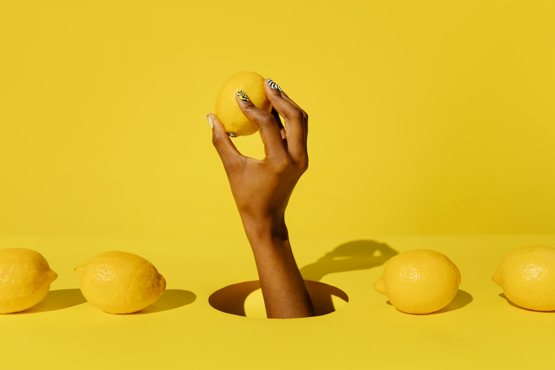 Una mano sosteniendo un limón fresco contra un fondo amarillo brillante, evocando frescura y vitalidad