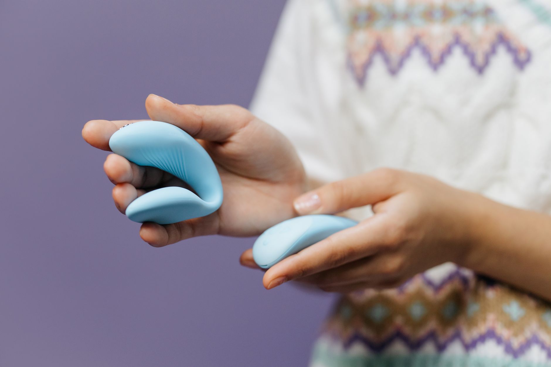 Mano sosteniéndose a un vibrador azul elegante contra un fondo púrpura, simbolizando placer e intimidad nuevos.