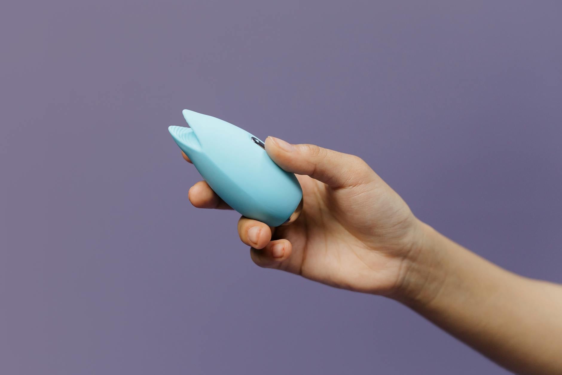 Vibrador de succión azul sostenido en la mano contra un fondo púrpura sólido