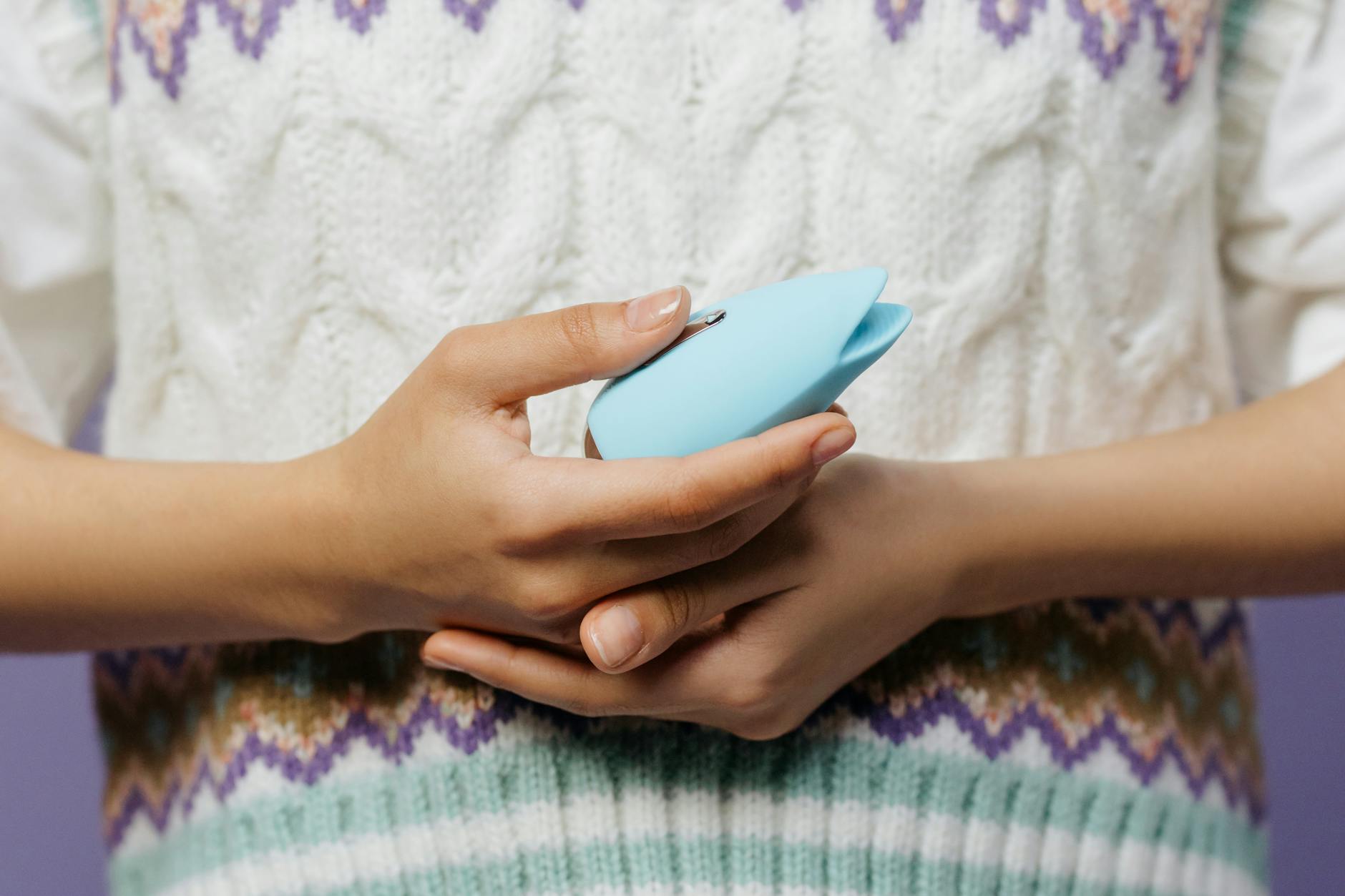 Hand holding a blue personal massager against a knitted sweater
